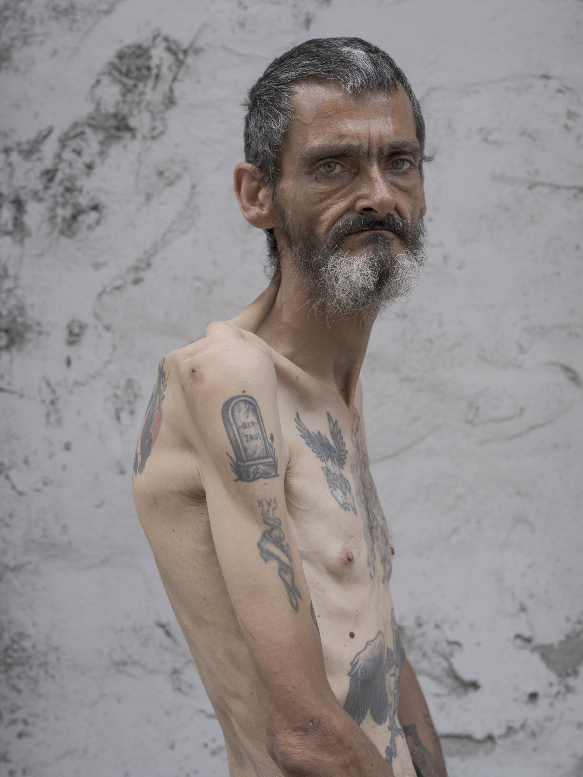 Retrato de hombre con barba y tatuajes frente a pared de piedra